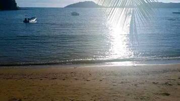 Una playa con aguas tranquilas, barcos y cielo despejado.