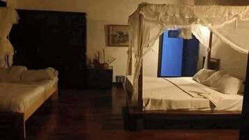 A room with two single beds, a wooden floor, a blue door, and a small table with a chair.