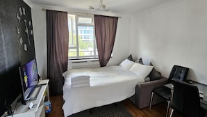 Een hotelkamer met een bed, een bureau met een computer, een stoel en een raam met gordijnen.
