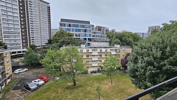 Een woongebied met meerlaags appartementencomplexen, een parkeerplaats met auto's en groene bomen.