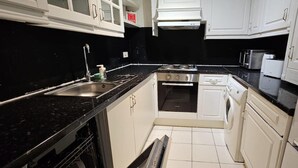 Een kleine keuken met witte kasten, een zwart aanrecht, een roestvrijstalen spoelbak, een ingebouwde oven, een vaatwasser en een magnetron.