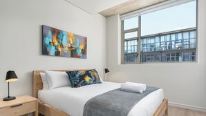 A modern bedroom with a wooden bed, a large window, and a colorful abstract painting on the wall. - Luxury 2 Bedroom Mountain Views (Cape Town)