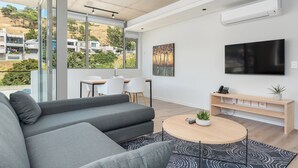 A modern living room with a grey sofa, a round wooden coffee table, and a flat-screen TV mounted on the wall. - Luxury 2 Bedroom Mountain Views (Cape Town)