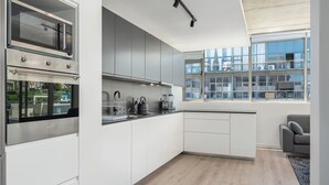 A modern kitchen with built-in appliances, a large window, and a grey sofa. - Luxury 2 Bedroom Mountain Views (Cape Town)
