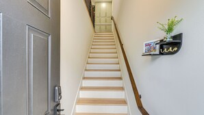 Una escalera de madera con barandilla metálica que lleva a una habitación con una puerta y un estante con una planta.