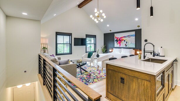Una sala de estar moderna con un sofá, una mesa de centro y un tapete colorido. Hay una zona de cocina con un fregadero y armarios.
