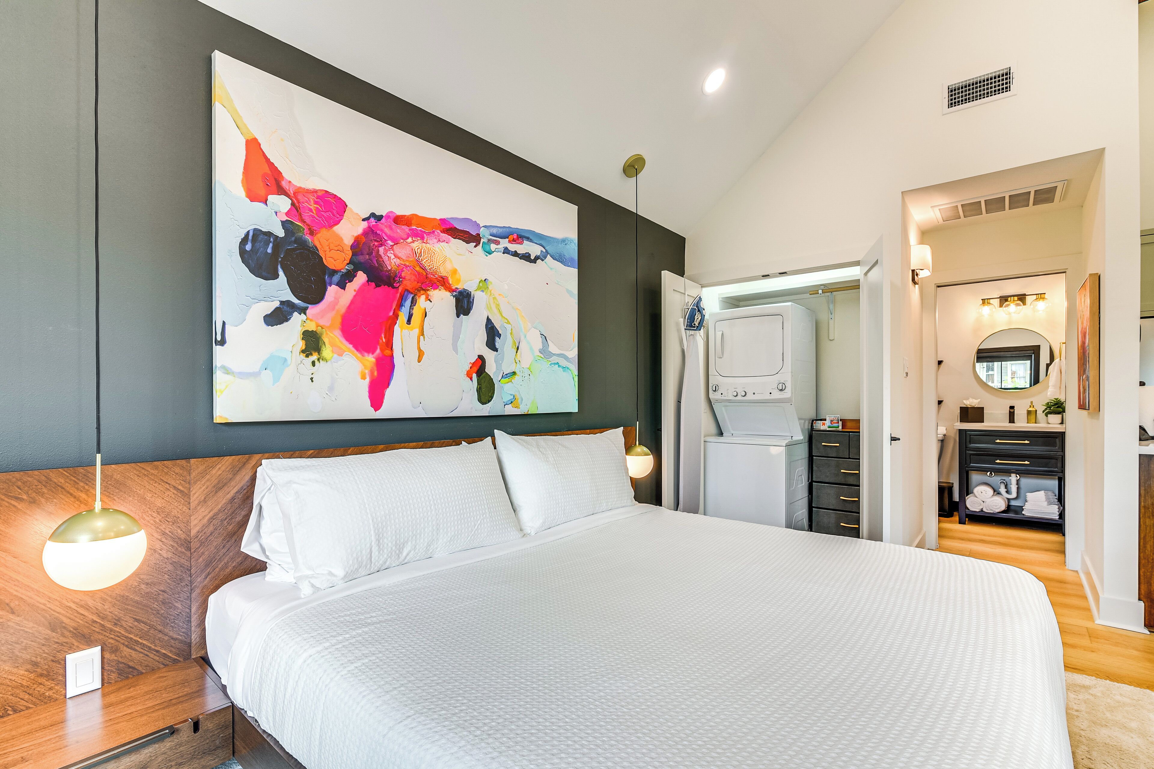 A modern bedroom with a large bed, a colorful abstract painting, a wooden headboard, and a walk-in closet.