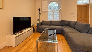 A living room with a flat-screen TV, a grey sofa, a glass coffee table, and a wooden floor. - Delightful 3BD Terrace House, Near London Bridge (Greater London)