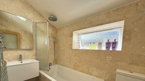 A bathroom with a bathtub, a toilet, a sink, and a window with toiletries. - Delightful 3BD Terrace House, Near London Bridge (Greater London)