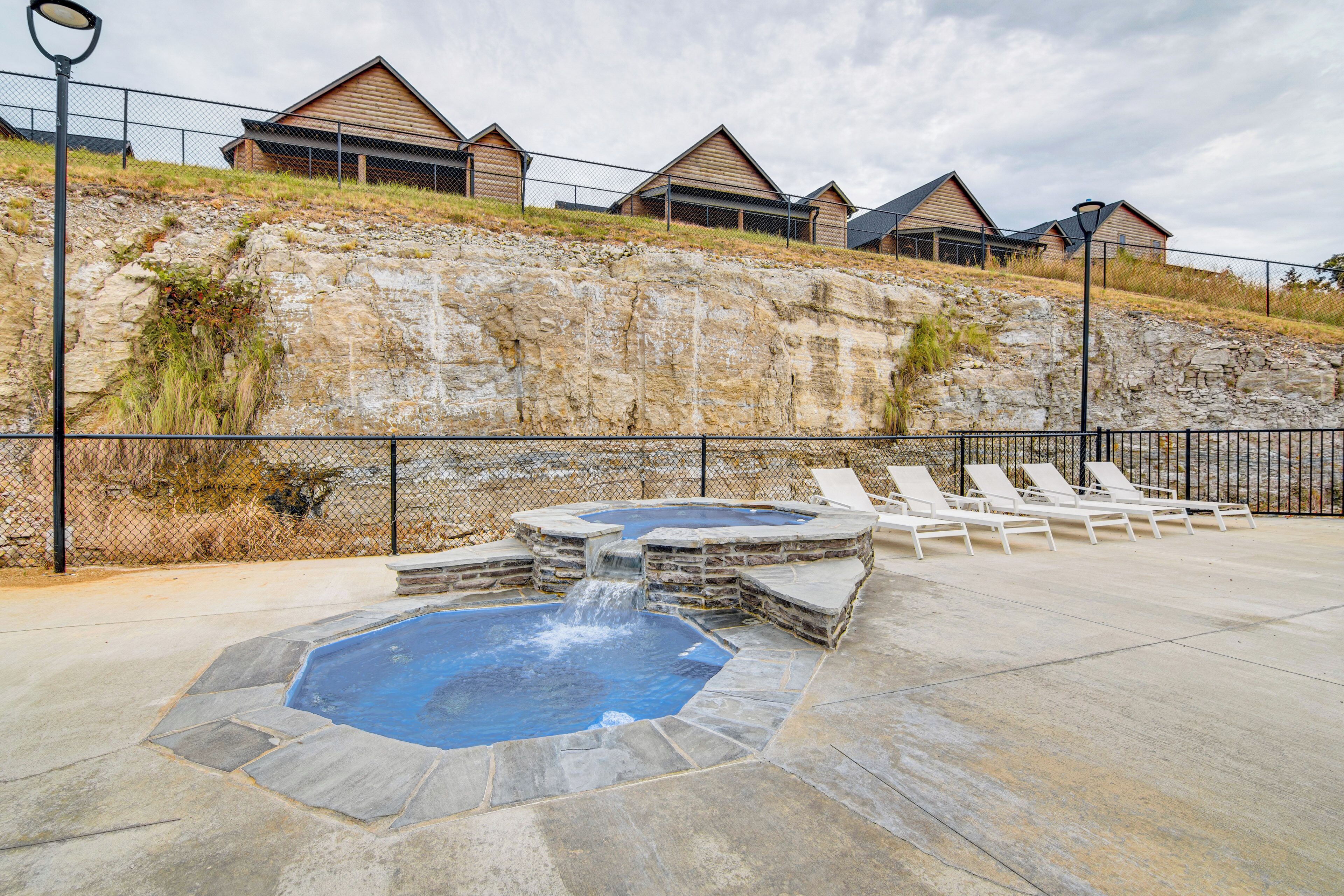 A swimming pool with a waterfall feature, surrounded by lounge chairs and a stone wall.