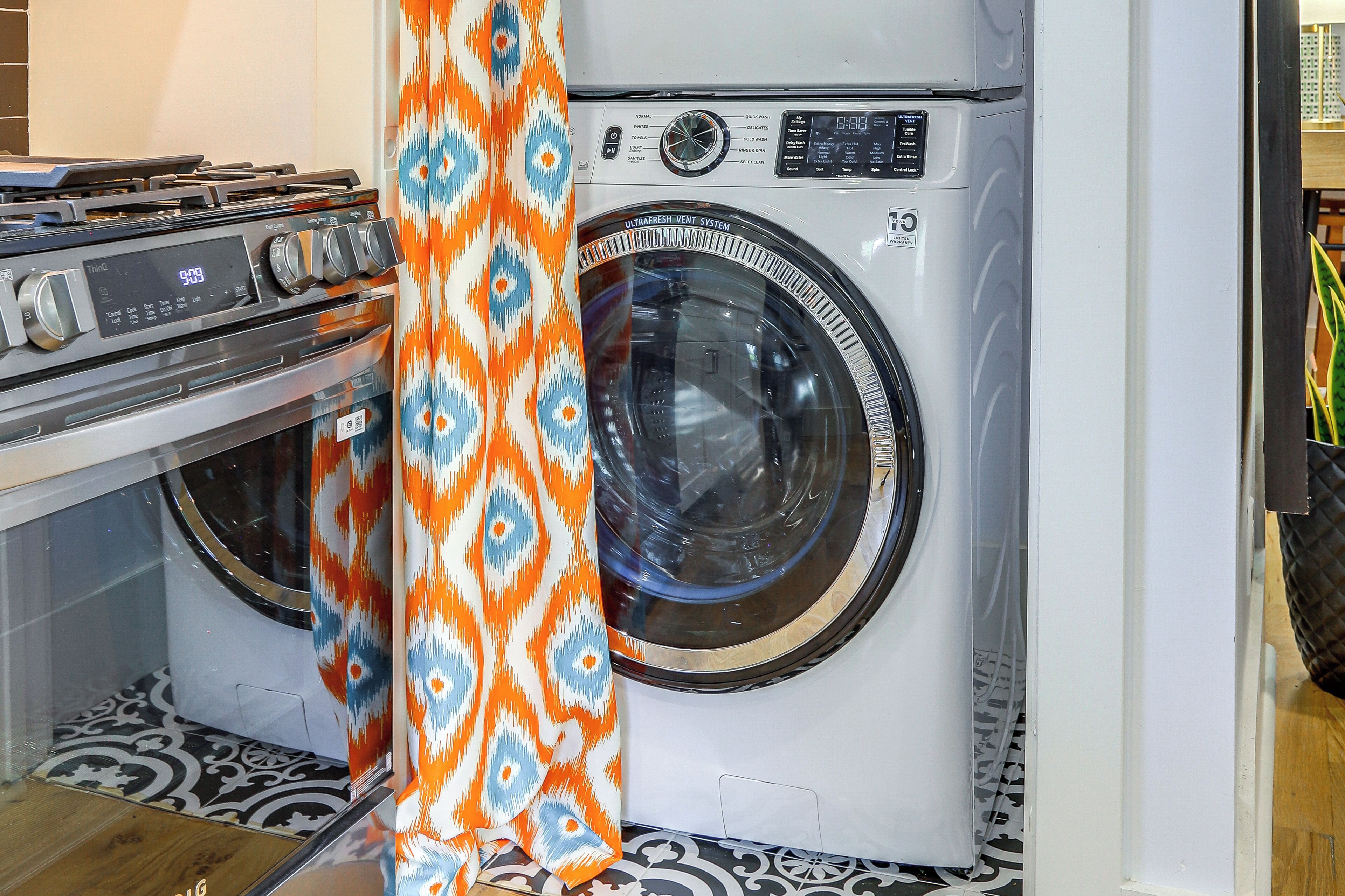 A laundry room with a washing machine and dryer, a patterned curtain, and a tiled floor.