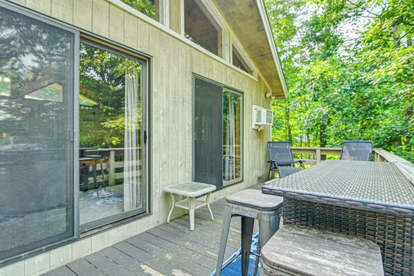 A covered outdoor patio with a table and chairs, a small white table, and a wicker chair. - Peaceful Highland Lake Home w/ Kayaks, Dock Access (Bridgton)