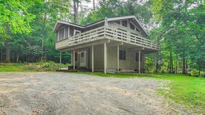 A two-story cabin with a balcony, surrounded by forest. - Peaceful Highland Lake Home w/ Kayaks, Dock Access (Bridgton)
