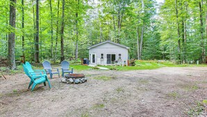 A cabin with a patio area, surrounded by a forest. - Quiet Pet Friendly Cabin w/ Fire Pit Near Lake Ann (Traverse City)