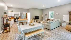 A modern kitchen with white cabinets, a dining table with a bench, a sofa, and a TV in the living area. - Quiet Pet Friendly Cabin w/ Fire Pit Near Lake Ann (Traverse City)