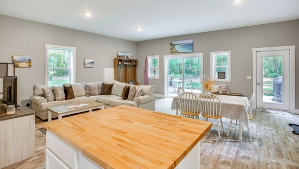 A spacious living area with a wooden dining table, a sofa, and a kitchen area with a countertop. - Quiet Pet Friendly Cabin w/ Fire Pit Near Lake Ann (Traverse City)