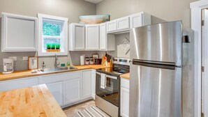A modern kitchen with white cabinets, stainless steel appliances, a wooden countertop, and a window with a view of greenery. - Quiet Pet Friendly Cabin w/ Fire Pit Near Lake Ann (Traverse City)