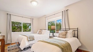 A bedroom with two beds, a window with curtains, a lamp, and a view of greenery outside. - Charming 3BR Villa, Heated Pool and BBQ | Solana 6 (Tucson)