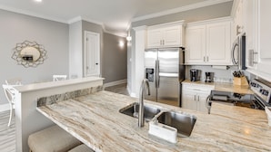 A modern kitchen with white cabinetry, a marble countertop, stainless steel appliances, and a breakfast bar.