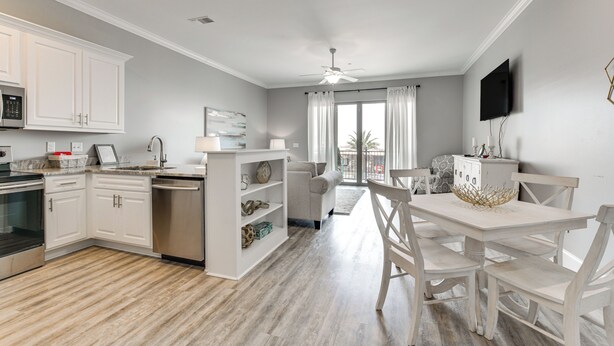 A modern kitchen with white cabinetry, a built-in oven, and a dishwasher. There is a dining area with a white table and chairs, and a ceiling fan above.