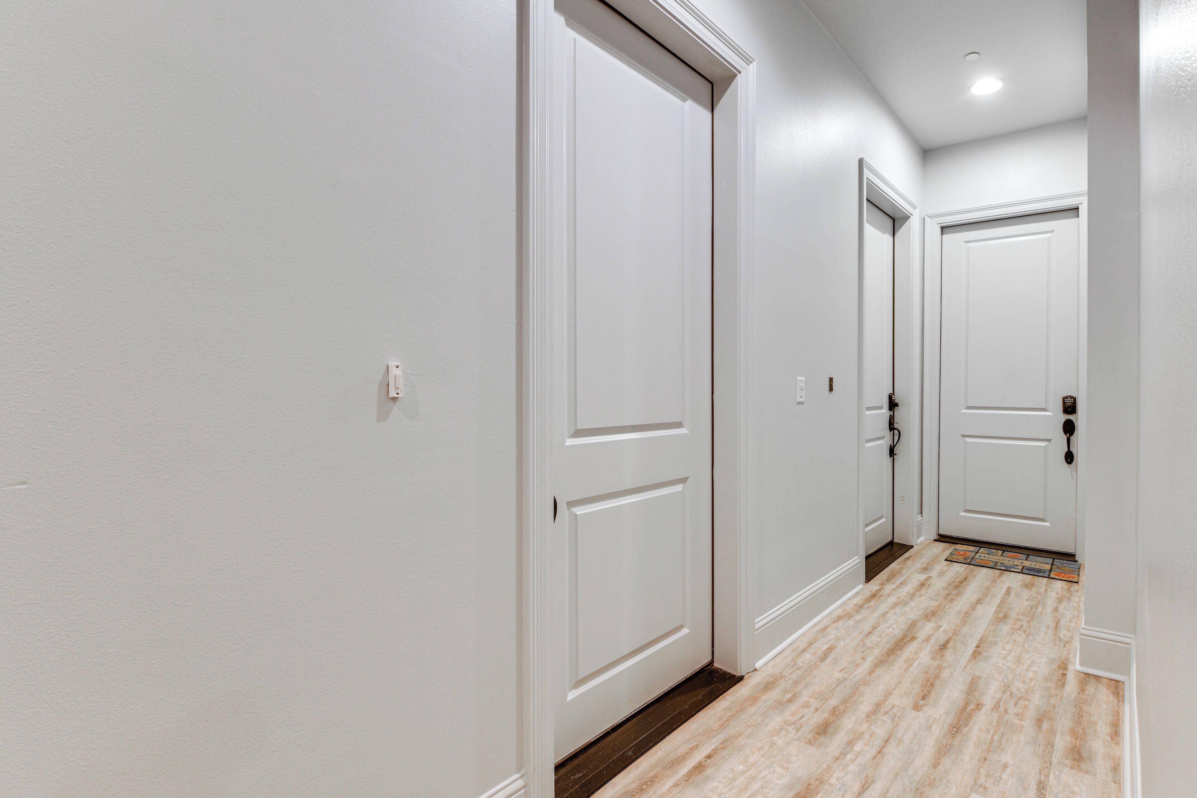 A hallway with white walls and wooden flooring, leading to three closed doors.