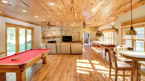 A wooden-floored room with a pool table, a stone wall, and a stone fireplace. - Sprawling Minnesota Home w/ On-site Lake Access (Nisswa)