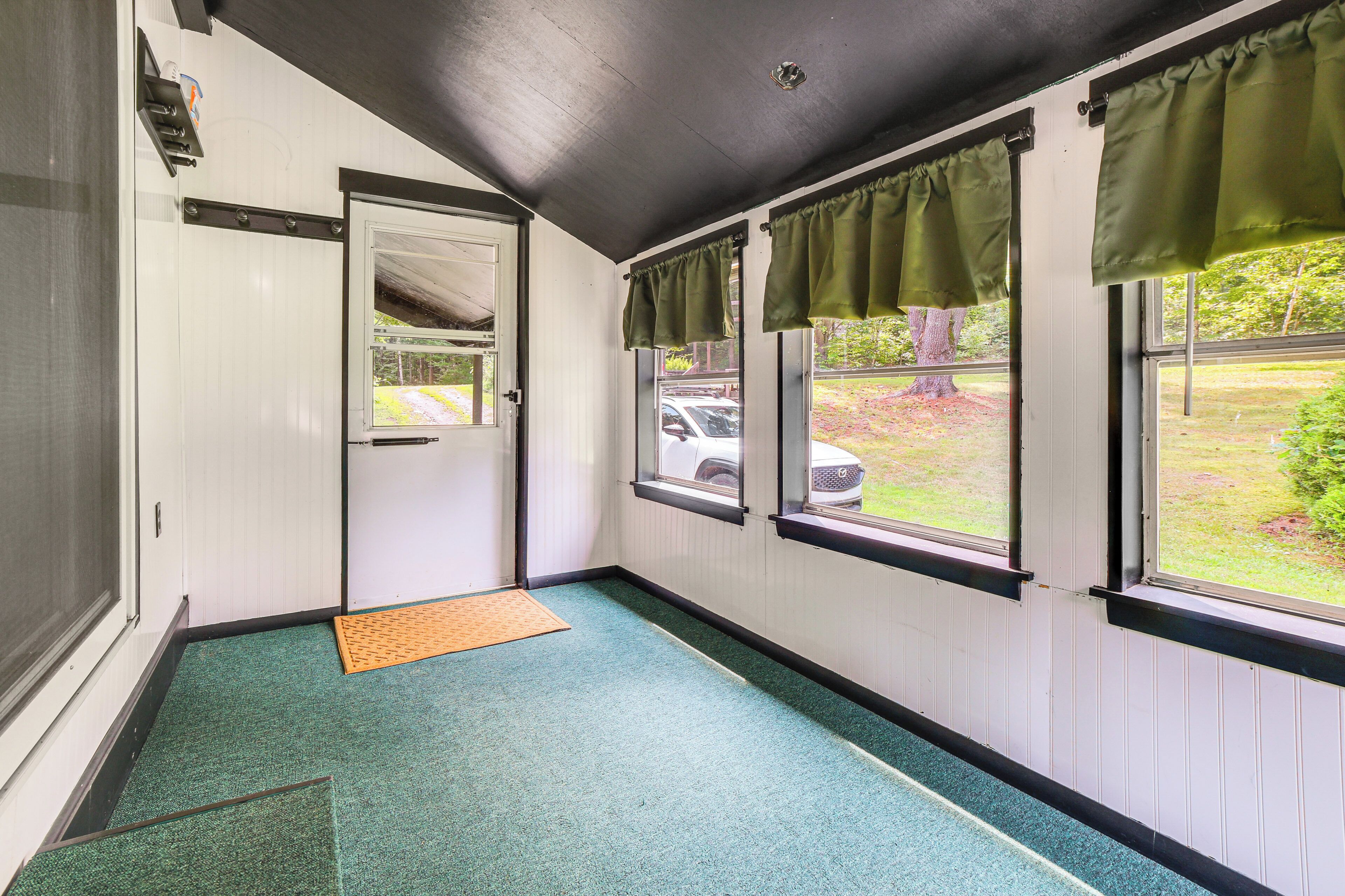 A hallway with a green carpet, a door, and windows with green valances.