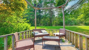 A wooden deck with wicker furniture, including a sofa and chairs, surrounded by lush greenery. - Peaceful Brookside Getaway ~10 Mi to Okemo Slopes! (Chester)