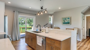 A modern kitchen with a large island, wooden cabinets, and a view of the outdoors. - Rock Hall Retreat w/ Balcony Near Park & Marina! (Rock Hall)
