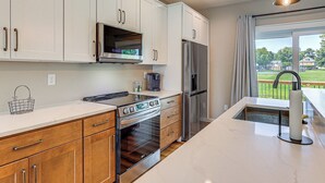 A modern kitchen with white cabinets, stainless steel appliances, and a large island with a sink. - Rock Hall Retreat w/ Balcony Near Park & Marina! (Rock Hall)