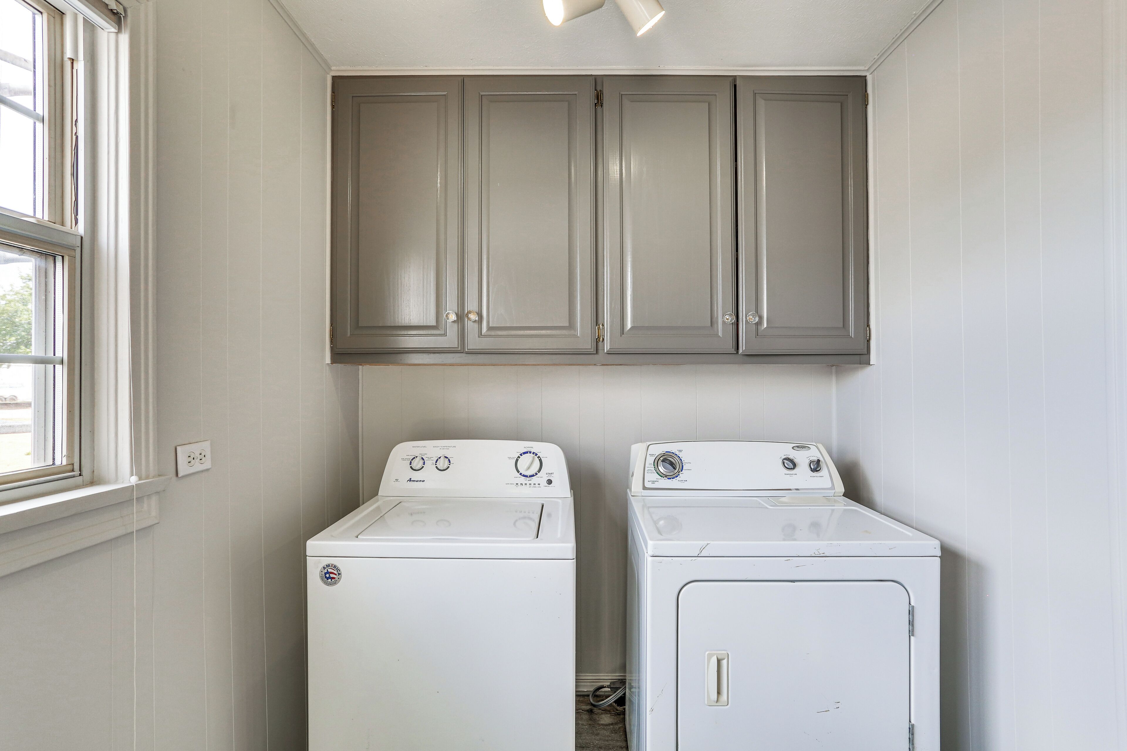 A laundry room with two white washing machines and gray cabinets above them.