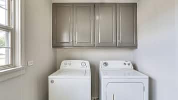 A laundry room with two white washing machines and gray cabinets above them.
