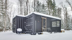 A modern, black cabin with a large window and a door, surrounded by snow-covered trees. - Nashwauk Studio w/ Ice Fishing on South Fork Lake (Nashwauk)