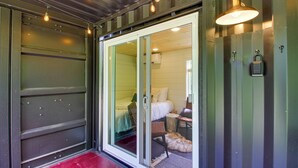 A room with a sliding glass door leading to a bed, a small table, and a furry rug on the floor. - Ice Fishing on South Fork Lake: Nashwauk Studio! (Nashwauk)
