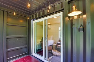 Una habitación con puerta corrediza de vidrio que da a una cama, una mesita pequeña y una alfombra mullida en el suelo.