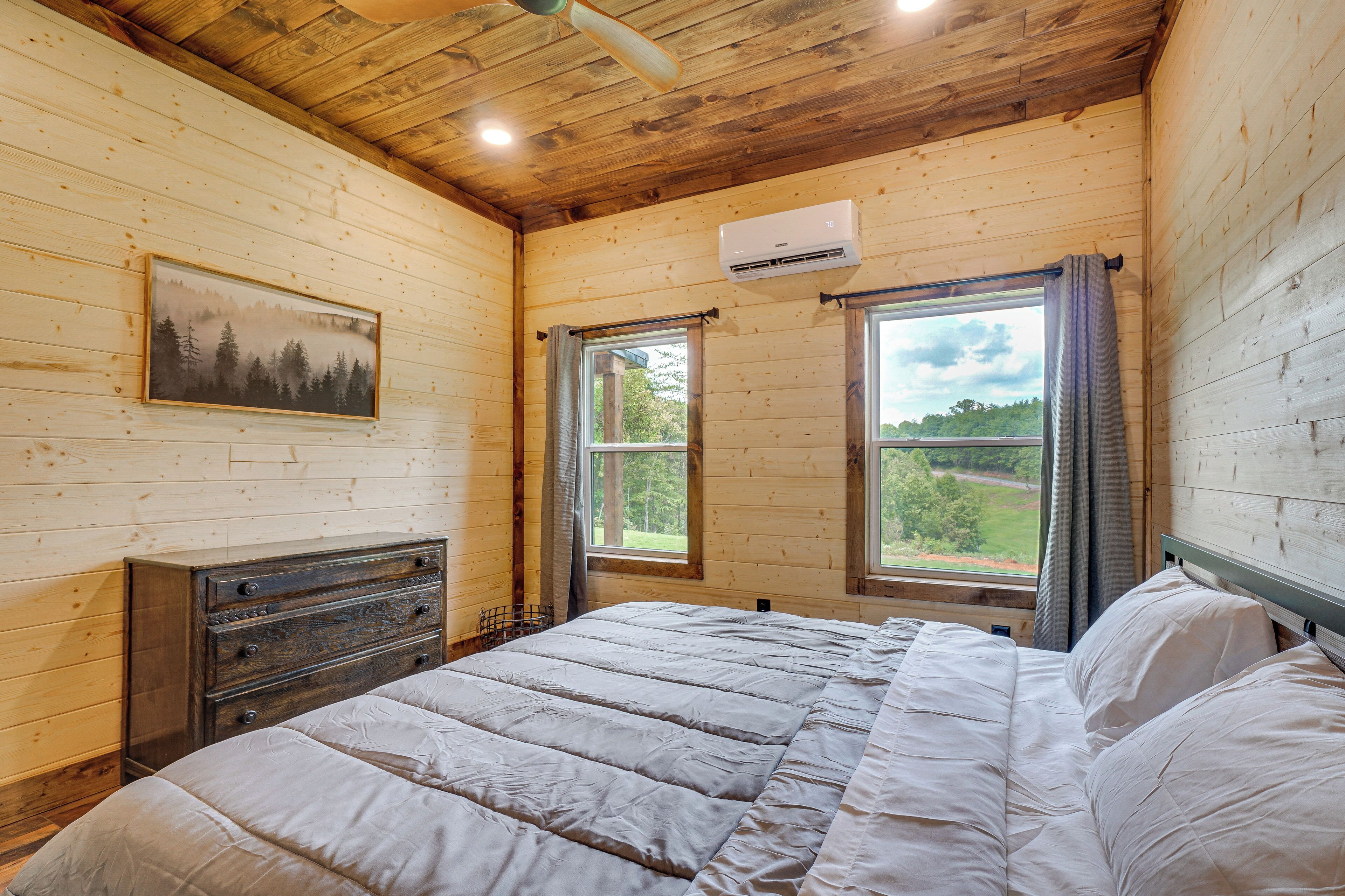 A wooden cabin bedroom with a bed, dresser, and a window with a view of the outdoors.