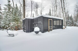 Un espacio exterior cubierto de nieve con una estructura de metal negro, posiblemente una cabaña o un depósito, rodeado de árboles cargados de nieve.