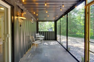 Un espacio al aire libre con techo, una mesa y sillas, ventanas grandes y luces colgantes.