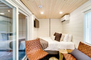 Un dormitorio con una cama, dos sillas tejidas, una pequeña mesa de madera y un televisor montado en la pared.