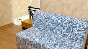 A room with a patterned sofa, a small wooden table, a chair, and a wall-mounted picture of a coastal scene. - San Martino House at the Cathedral (Catania)
