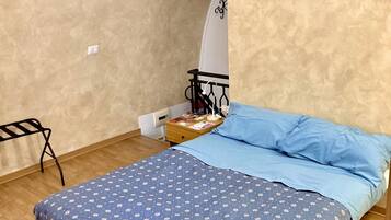 A bedroom with a bed, a small table with a lamp, a chair, and a picture on the wall.