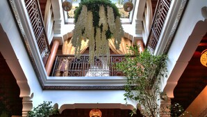 Un vaste atrium agrémenté de balustrades en fer forgé ouvragé, de décorations florales suspendues et d’un balcon central offrant une vue sur le ciel.