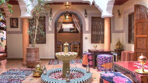 Un intérieur marocain traditionnel agrémenté d’une fontaine, de tapis à motifs et de meubles richement décorés.