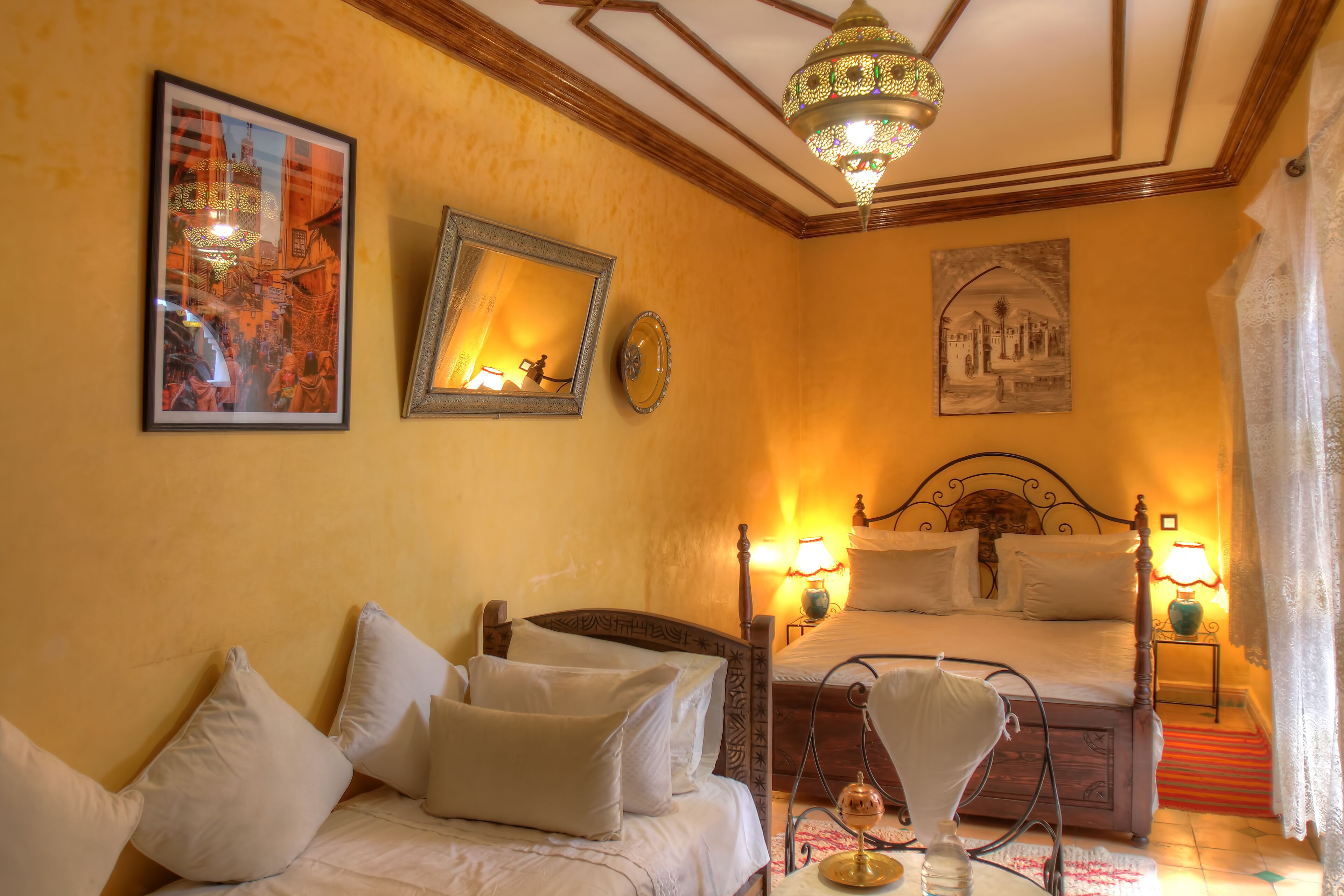 A hotel room with two beds, a sofa, a chandelier, and artwork on the walls.
