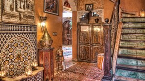 Un couloir richement décoré, orné de motifs complexes en mosaïque, avec un magnifique escalier et de somptueuses portes en bois sculpté.