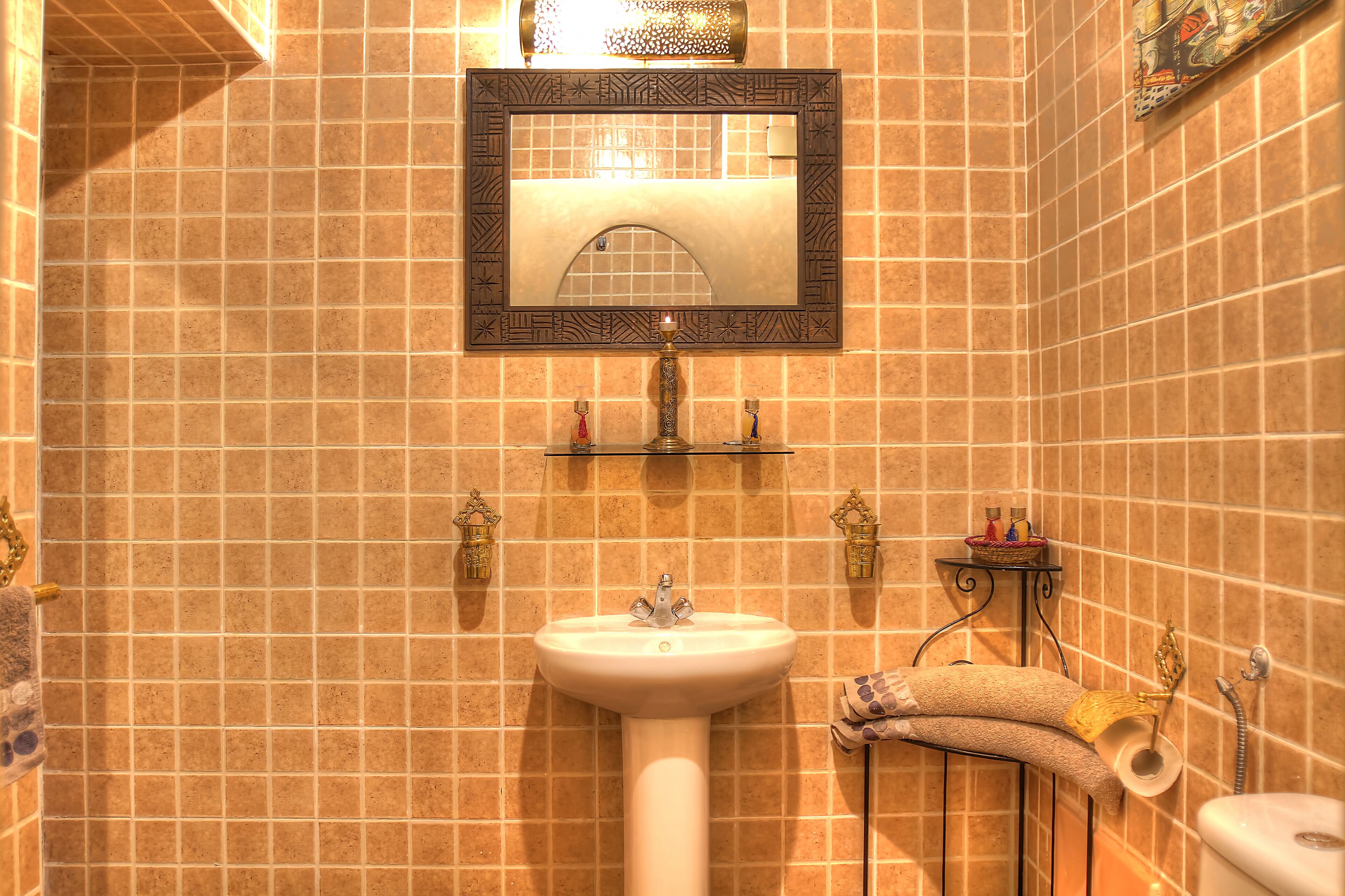 Une salle de bain avec un lavabo blanc, un miroir doté d’un cadre décoratif et un porte-serviettes sur lequel est posée une serviette.