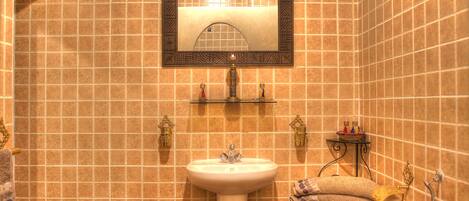 Une salle de bain avec un lavabo blanc, un miroir doté d’un cadre décoratif et un porte-serviettes sur lequel est posée une serviette.