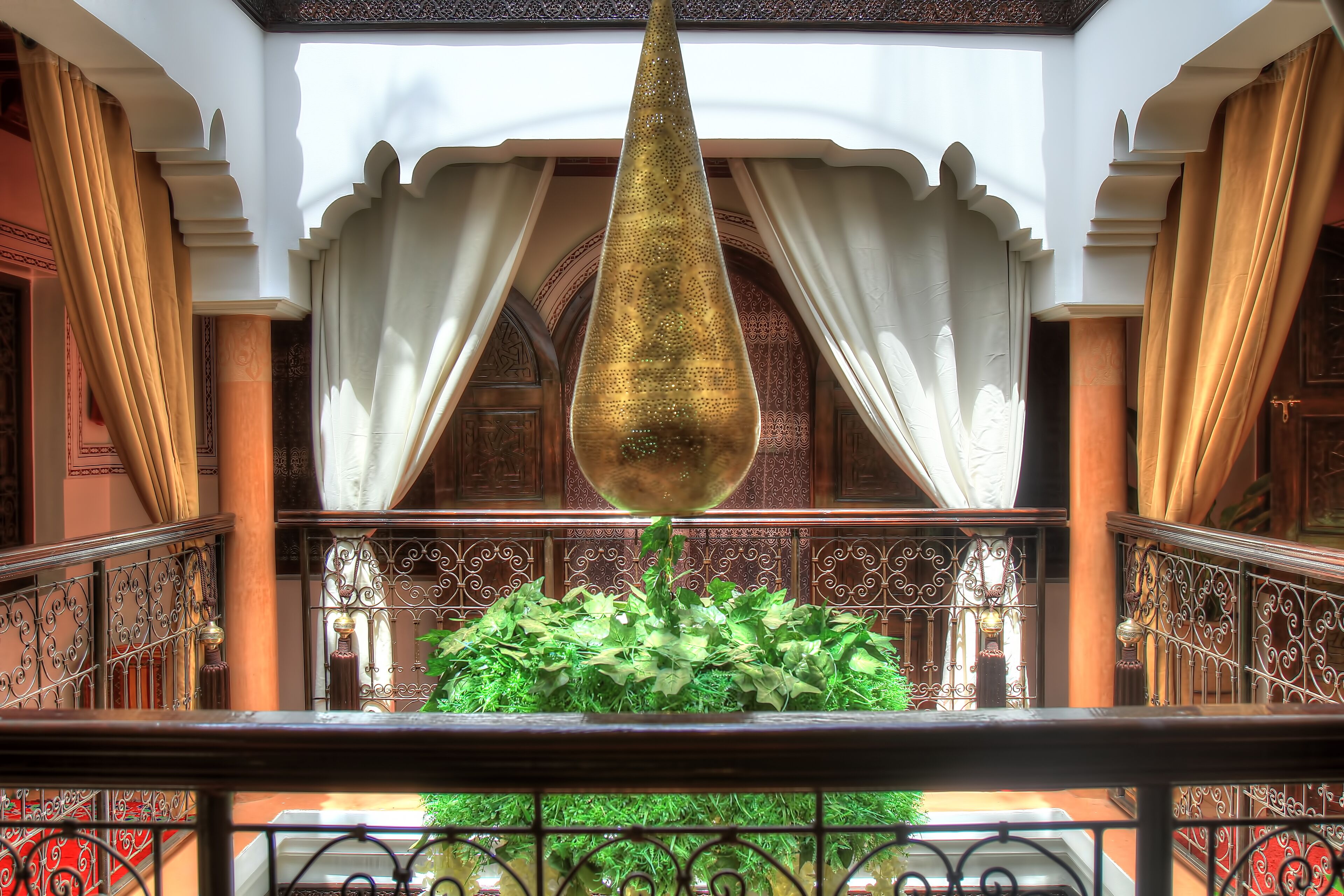 A balcony with a hanging ornament, ornate railings, and a lush green plant arrangement.
