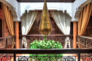 A balcony with a hanging ornament, ornate railings, and a lush green plant arrangement.