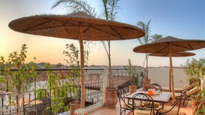 Une terrasse avec des espaces de détente en plein air, comprenant des tables et des chaises, entourée de plantes en pot et de parasols.
